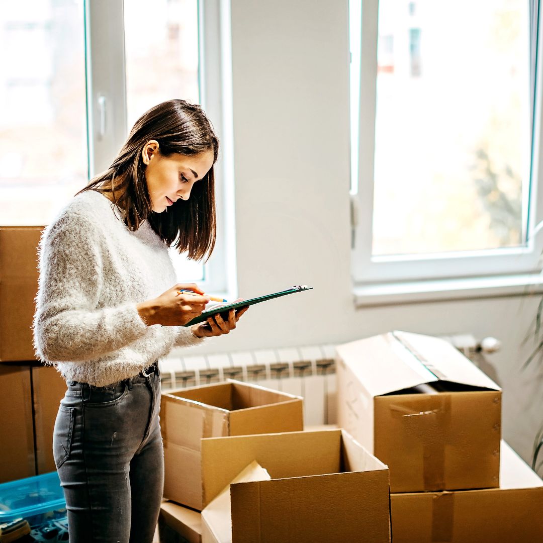 Woman checking clipboard next to pile of boxes